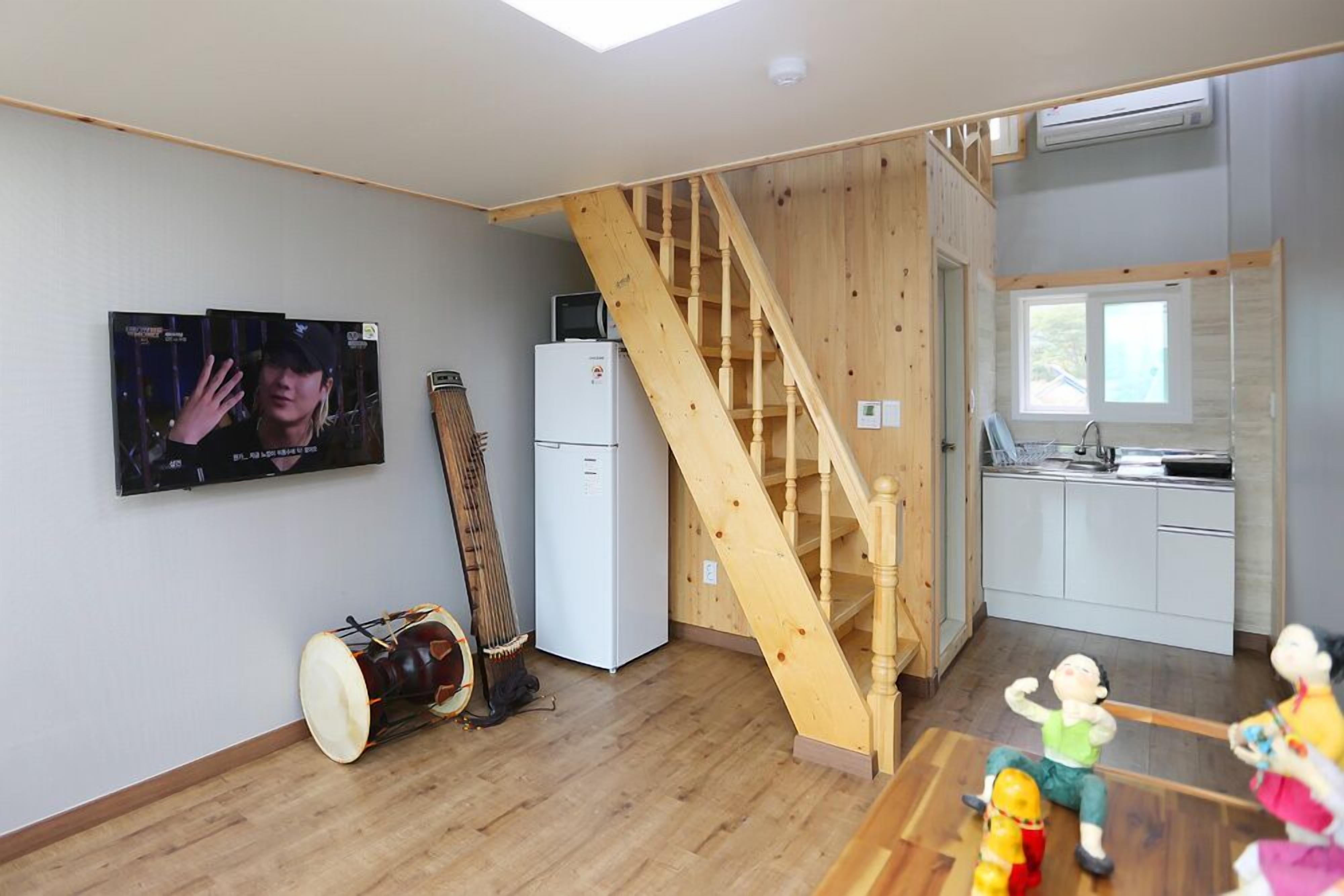 A modern kitchen with a wooden staircase, a television mounted on the wall, and a refrigerator.