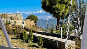 A view from a covered porch overlooking a stone wall, a small building, and a mountainous landscape. - BSR Farms (Pauri)
