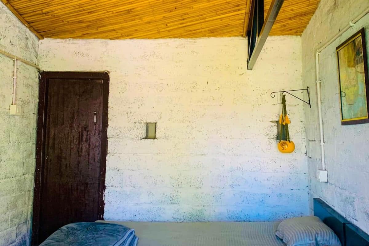 Una habitación con dos camas, techo de madera, una puerta y una lámpara.