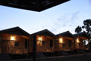 A row of wooden cabins with open porches and a clear sky in the background. - BSR Farms (Pauri)