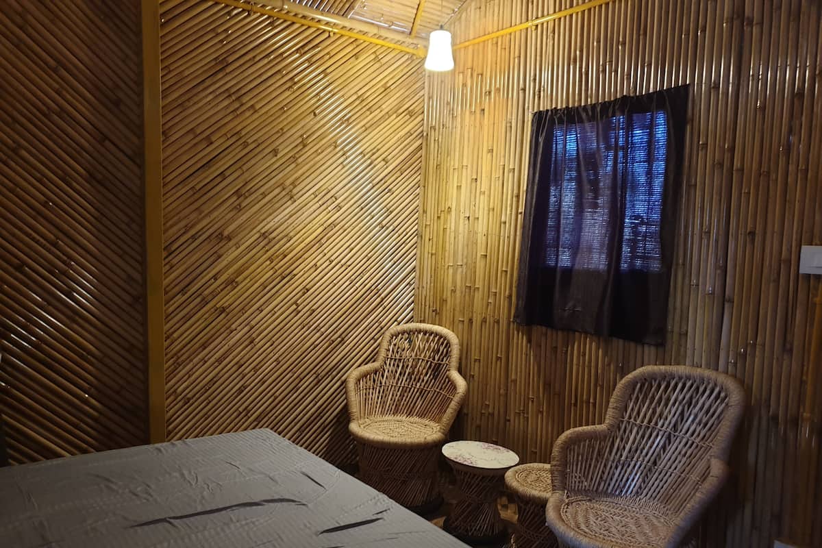 Una habitación con una cama, dos sillas de mimbre, una mesita redonda y un televisor fijado a la pared.