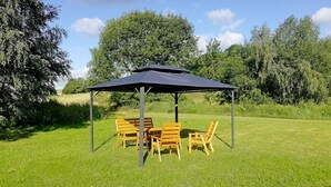 Un belvédère avec une table et des chaises, installé dans un espace verdoyant.