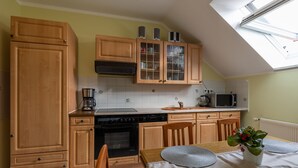Une cuisine avec des meubles en bois, un four à micro-ondes, une cuisinière et une table à manger agrémentée de sets de table et d’une plante en pot.