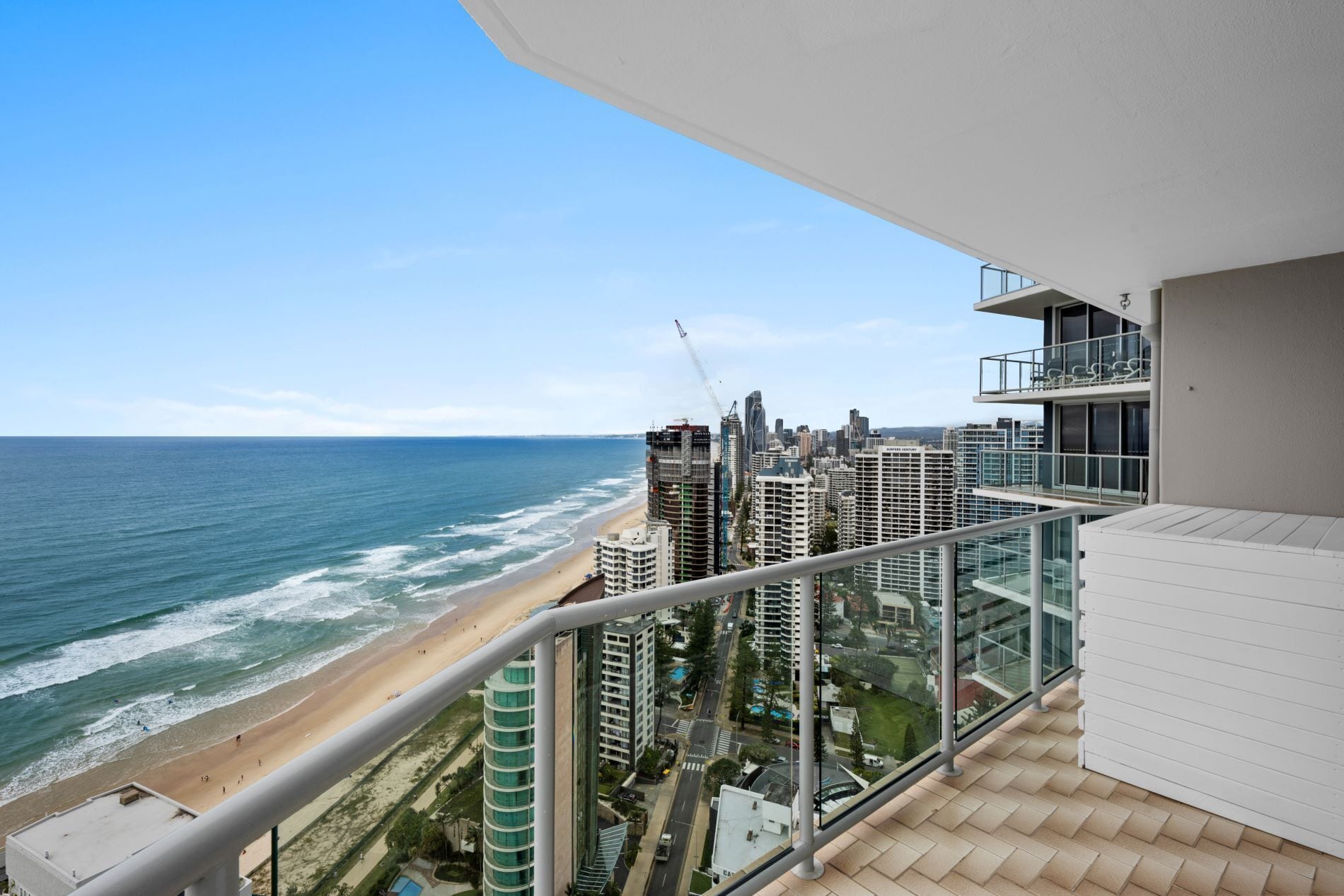 A balcony with a view of the beach and ocean, overlooking a cityscape with high-rise buildings.