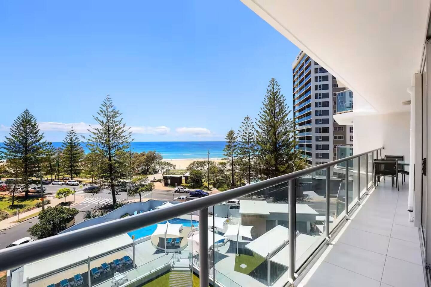 Un balcón con vistas a la playa, un área de piscina y un edificio alto al fondo.