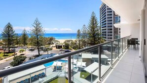 A balcony with a view of the beach, a pool area, and a tall building in the background. - Peninsula Resort - Private Apartments (Surfers Paradise)