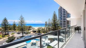 Un balcón con vistas a la playa, un área de piscina y un edificio alto al fondo.
