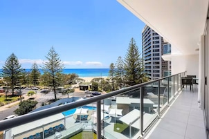 Un balcón con vistas a la playa, un área de piscina y un edificio alto al fondo.