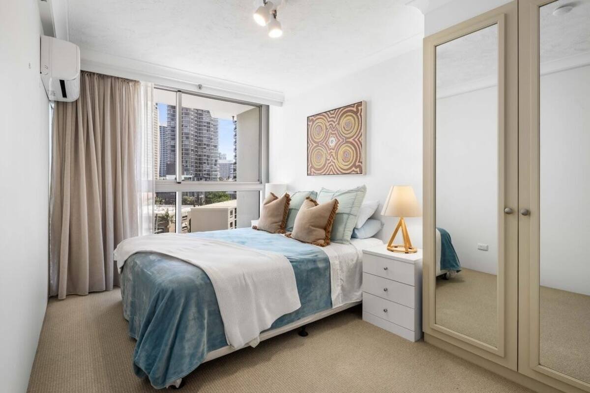 A bedroom with a bed, bedside table, lamp, and a large mirror.