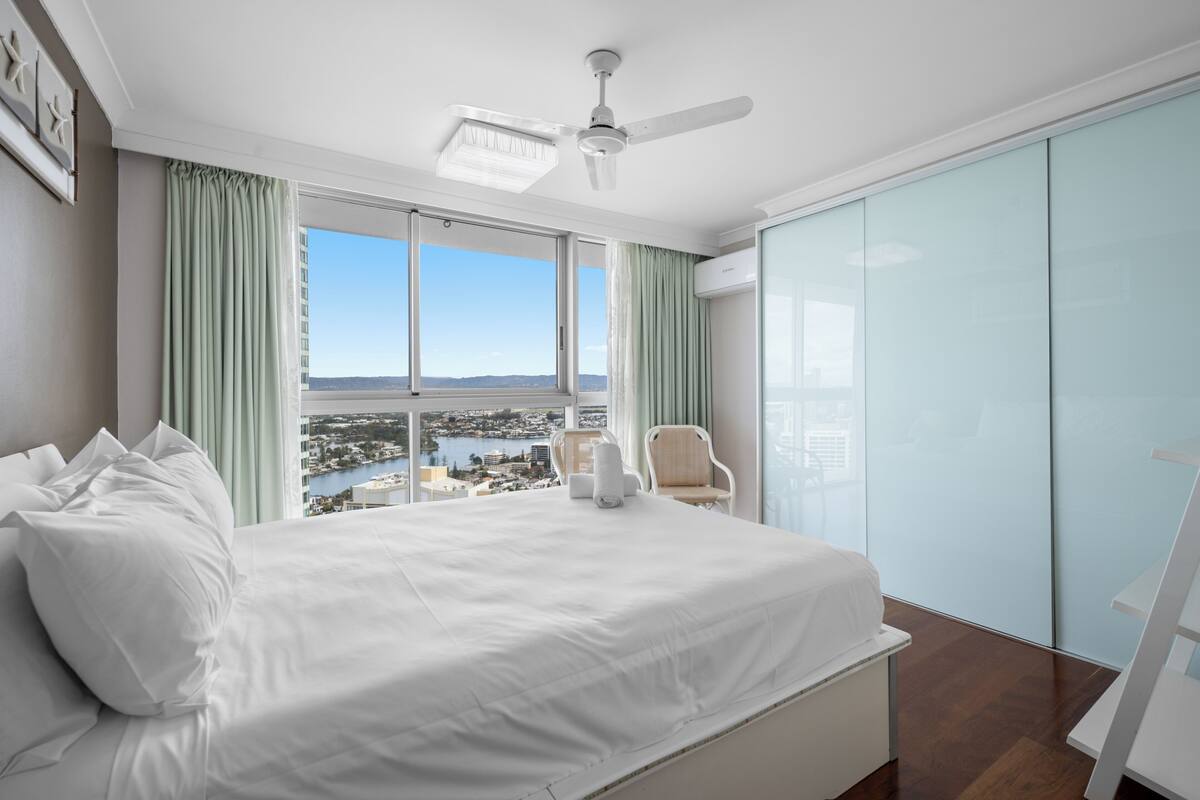 A hotel room with a large bed, a ceiling fan, a view of a cityscape, and a sliding glass door.