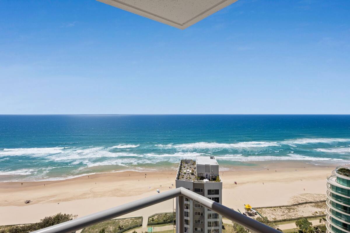 A beach view from a balcony with a clear sky, sandy beach, and ocean waves.