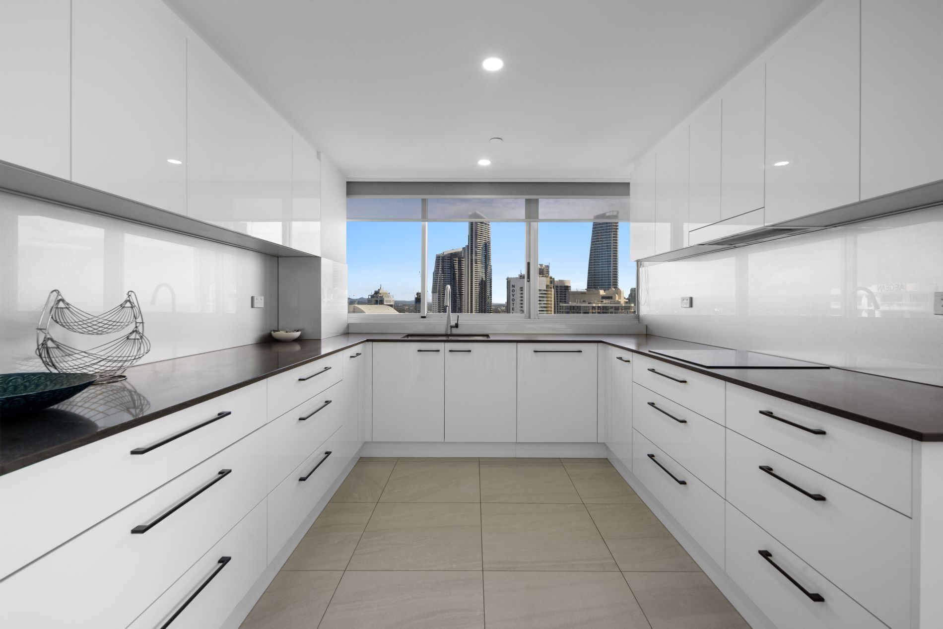 Una cocina moderna con armarios blancos, encimeras negras y vistas a rascacielos.