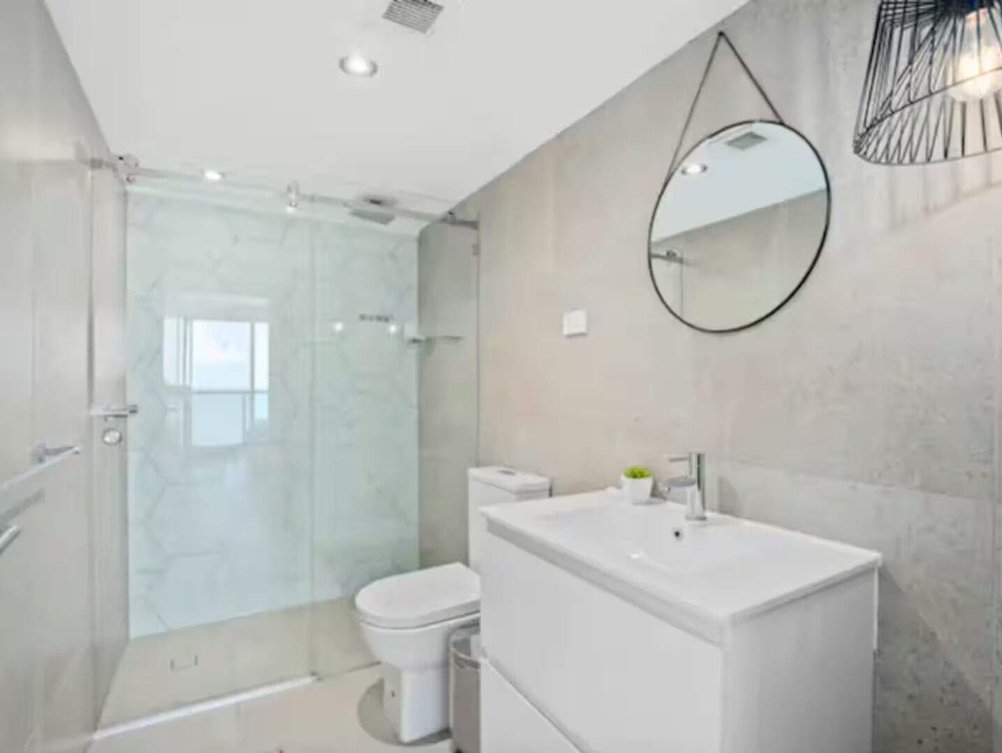 A modern bathroom with a glass shower enclosure, a white toilet, and a large rectangular sink with a mirror above it.