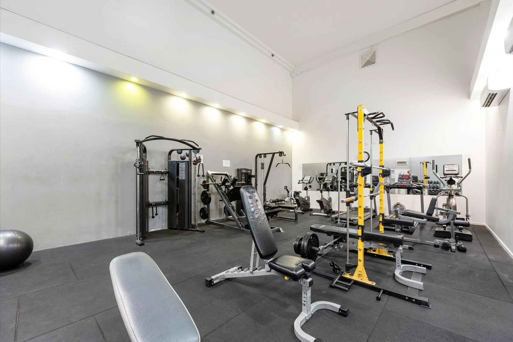 Ein Fitnessstudio mit unterschiedlichen Trainingsgeräten, darunter Bänke, Kraftgeräte und ein Squat-Gestell.