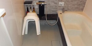 A bathroom with a bathtub, a white stool, and a shower area with multiple bottles.