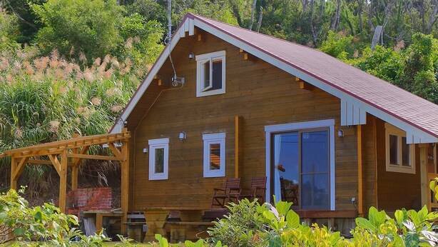 Une cabane en bois avec un toit à pignon, une véranda avec des chaises et une pergola en bois.