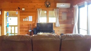L’intérieur d’une cabine est aménagé avec du bois, il y a un canapé, un téléviseur et une fenêtre avec des rideaux.