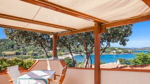 A covered outdoor seating area with a table and chairs, overlooking a scenic coastal landscape. - Holiday Apartment "Corbezzoli" with Sea View, Wi-Fi, Balcony, Garden & Terrace (San Teodoro)