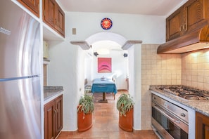 Una cocina con un refrigerador de acero inoxidable, armarios de madera, una estufa a gas y un comedor con una mesa y sillas.