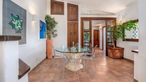 A dining area with a glass table and chairs, wooden cabinets, and potted plants. - Holiday Apartment "Corbezzoli" with Sea View, Wi-Fi, Balcony, Garden & Terrace (San Teodoro)