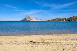 Una playa con aguas azul cristalino, una gran formación rocosa y una orilla arenosa.