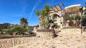 A stone building with a balcony, surrounded by palm trees and a stone wall. - Holiday Apartment "Corbezzoli" with Sea View, Wi-Fi, Balcony, Garden & Terrace (San Teodoro)
