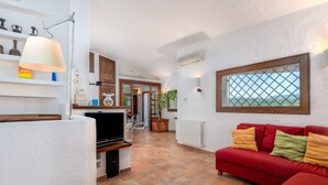 A living room with a red sofa, a television, and a lamp. There is a window with a view of greenery. - Holiday Apartment "Corbezzoli" with Sea View, Wi-Fi, Balcony, Garden & Terrace (San Teodoro)