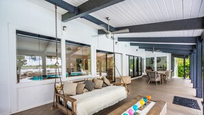 Un'ampia area interna con una poltrona a dondolo, un tavolo da pranzo e vista su una piscina esterna.