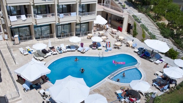 Une piscine sur le toit, dotée de chaises longues et de parasols, et entourée d’un immeuble à plusieurs étages avec des balcons.