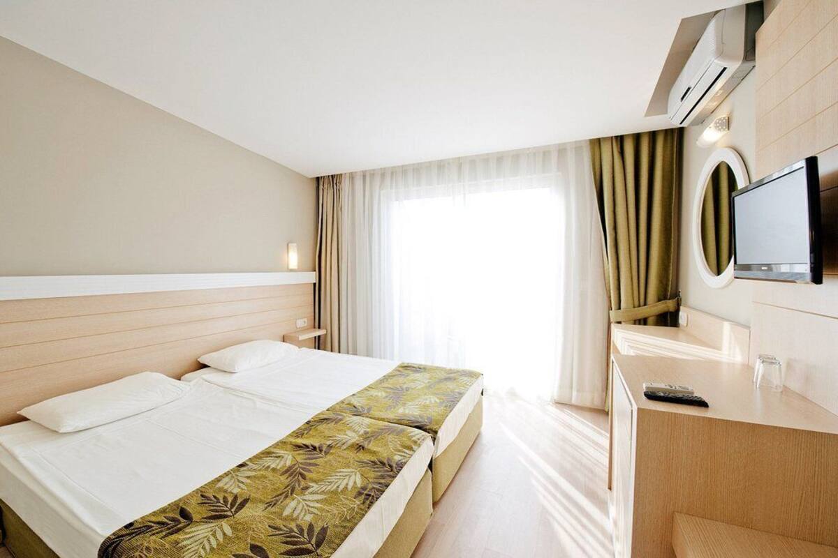 Een hotelkamer met een bed, een bureau, een televisie en een raam met gordijnen.