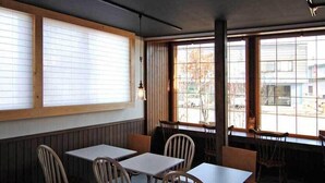 A restaurant interior with wooden paneled walls, large windows with blinds, and simple table and chair arrangements. - Sapporo Guest House Anne - Hostel (Sapporo)