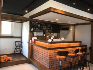 A cafe with a brick counter, a chalkboard menu, and bar stools. - Sapporo Guest House Anne - Hostel (Sapporo)