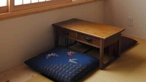A traditional Japanese room with tatami flooring, a low wooden table, a blue cushion, and a sliding shoji screen. - Sapporo Guest House Anne - Hostel (Sapporo)