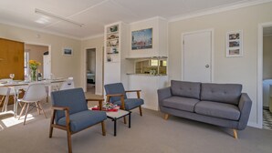 Ein Wohnzimmer mit grauem Sofa, zwei blauen Sesseln, einem kleinen Couchtisch und einem Essbereich mit weißem Tisch und Stühlen.