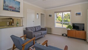 Ein Wohnzimmer mit grauem Sofa, Holzstühlen, einem Fernseher auf einem Holzschrank und einem Bild an der Wand.