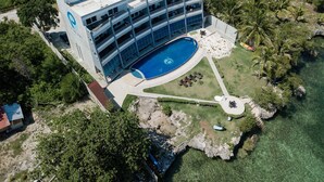 Et hotel med flere etager, en swimmingpool og frodig vegetation samt klart vand.