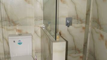 Un baño con inodoro, cabina de ducha de vidrio y pared de mármol.