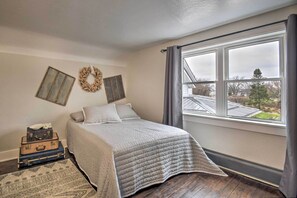 A bedroom with a bed, a window with curtains, a wall-mounted wreath, and a suitcase on the floor. - Charming Dairy Farm Home in Indiana Amish Country (Shipshewana)