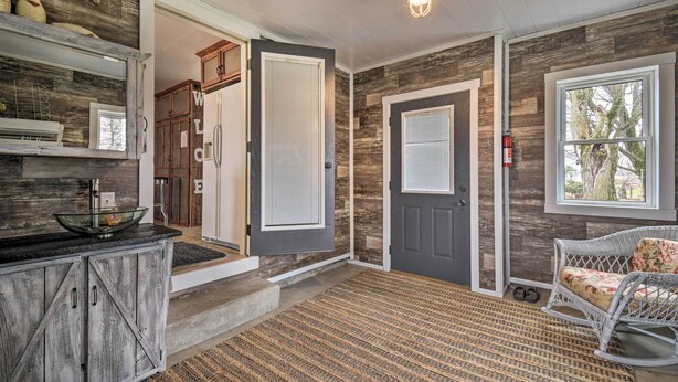 A rustic interior with a wooden floor, a glass bowl on a black countertop, a wicker rocking chair, and a door with a window view. - Charming Dairy Farm Home in Indiana Amish Country (Shipshewana)