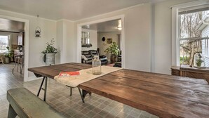 A spacious kitchen with a large wooden table, a dining bench, and a view of the living area through an open doorway. - Charming Dairy Farm Home in Indiana Amish Country (Shipshewana)