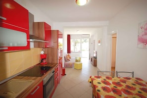 Een compacte keuken met moderne apparatuur, een eethoek met een tafel en stoelen, en een woonruimte met een bank en een raam.