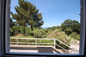 Een balkon met een hekwerk, met uitzicht op een tuin met verschillende bomen en struiken, en een helder zicht op de lucht.