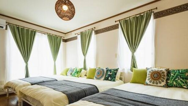 Ein Hotelzimmer mit zwei Betten, grünen Vorhängen und einer dekorativen Deckenleuchte.