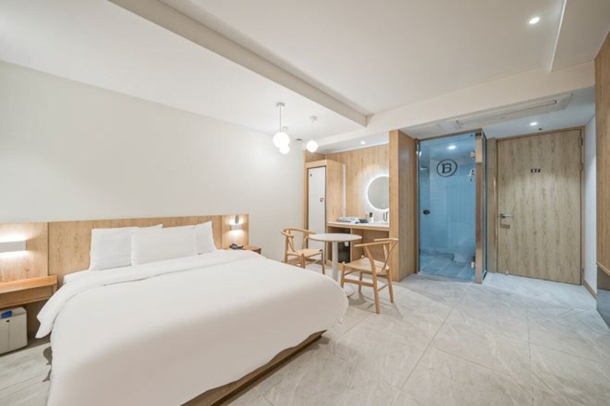Una habitación de hotel moderna con una cama grande, un escritorio con silla, un espejo redondo y una puerta de madera.