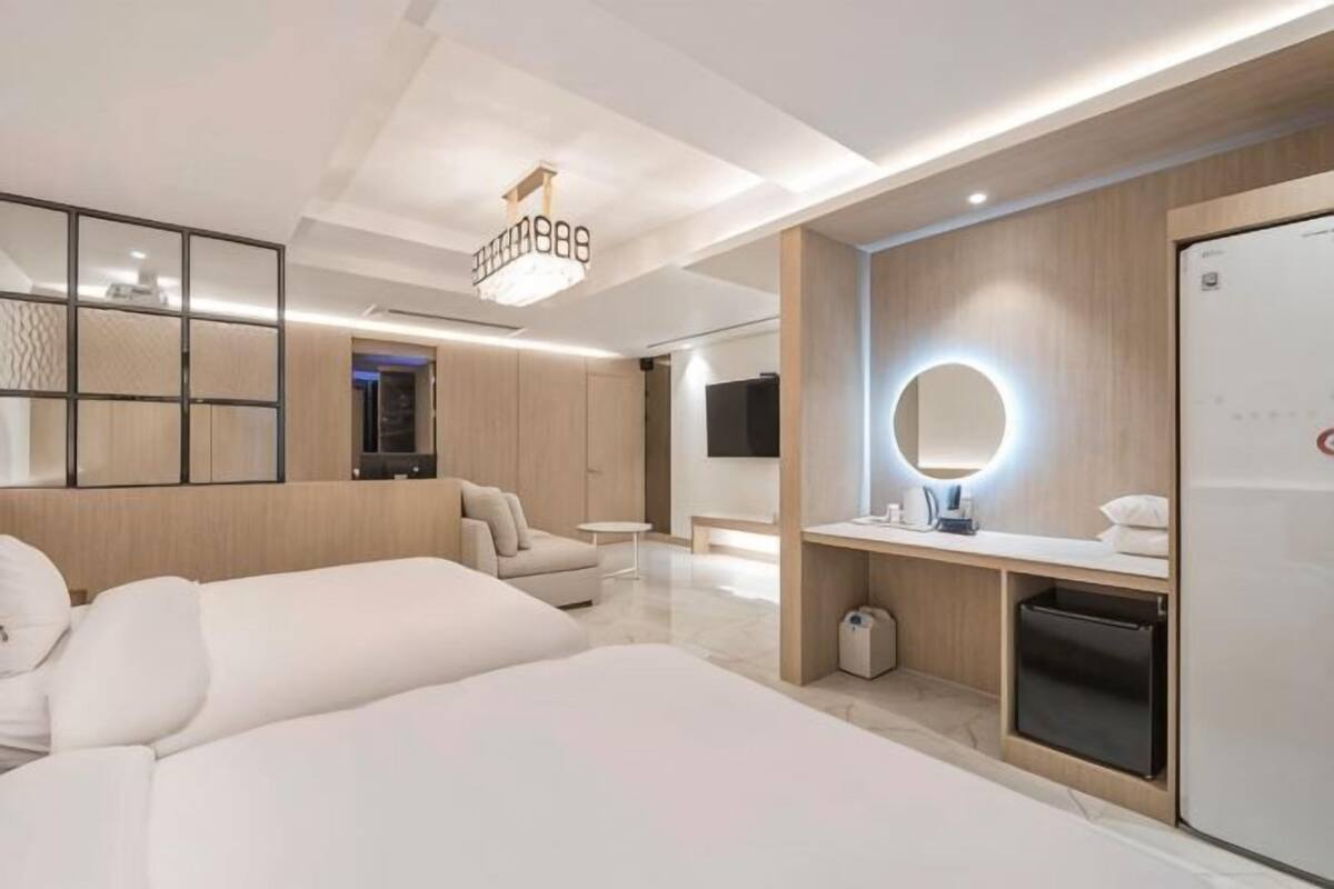A modern hotel room with two beds, a vanity with a mirror, a television, and a minibar.