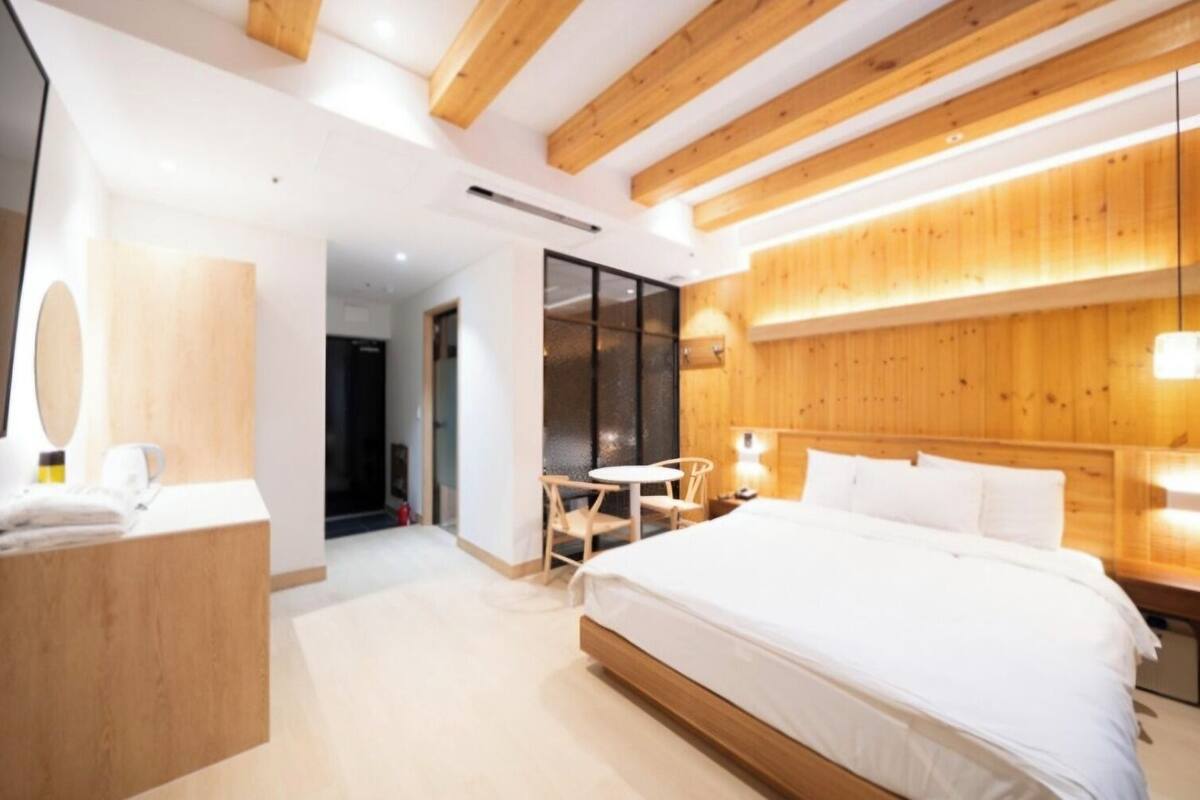 A modern hotel room with a wooden ceiling, a large bed, a desk with a chair, and a small table.