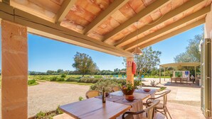 An outdoor patio with a wooden table and chairs, a potted plant, and a view of the countryside.