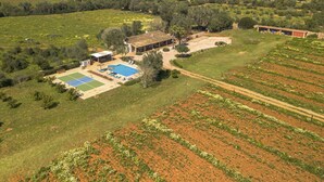 An aerial view of a property with a swimming pool, tennis courts, and adjacent fields.