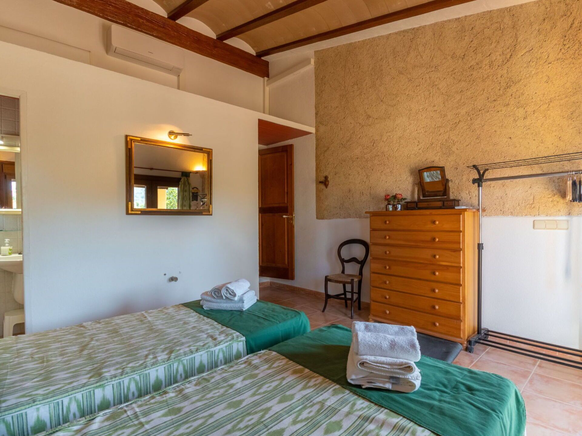 Une chambre avec deux lits, une commode en bois, un miroir et une chaise.