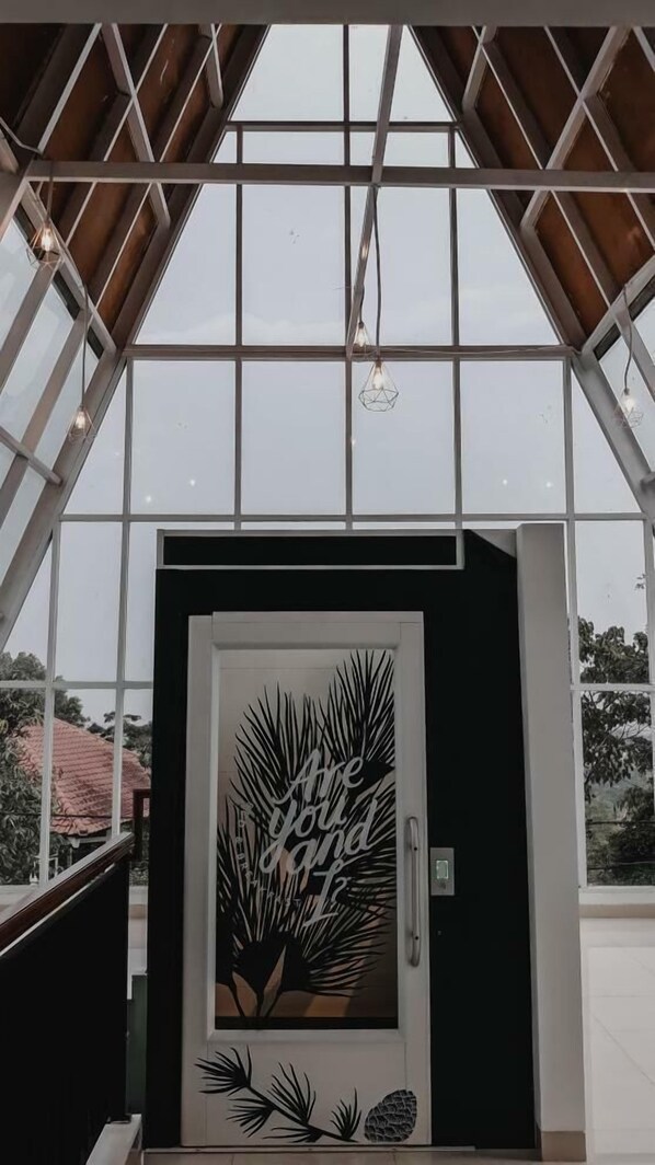 Una entrada de edificio moderna con un gran ventanal, un techo metálico geométrico y un letrero decorativo con hojas de palmera y texto.